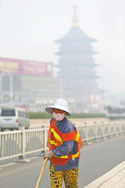 近日，在古都洛陽，環(huán)衛(wèi)工人身后的“天堂”被霧霾籠罩著。