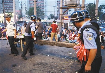 6月13日晚8點，朝陽路和青年路交叉口西側，一次聯(lián)合執(zhí)法行動中，輔警與協(xié)管抬走商戶的燒烤用具。新京報記者 尹亞飛 攝