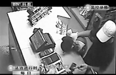 戴帽男子一手掐住加油站營(yíng)業(yè)員，一手持發(fā)令槍指向另一營(yíng)業(yè)員，要求“把錢給我裝起來”。