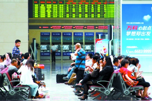 候車大廳溫度很高，一名乘客一手扇風(fēng)、一手擦汗