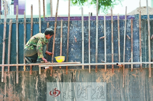 　　烈日下，狹窄的架子上，工人正用錘子固定樁基。