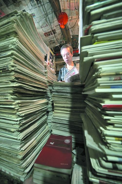 王曉民坐在寫(xiě)字桌前，被報(bào)紙淹沒(méi)。