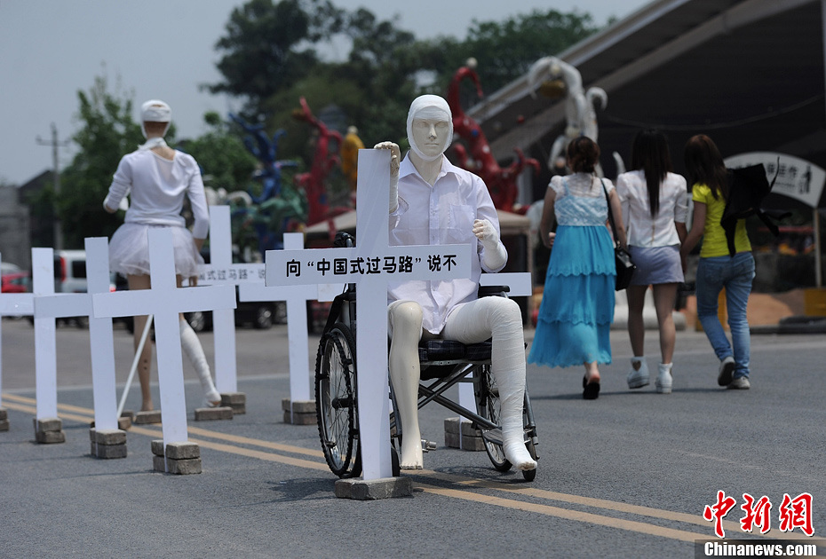 4月16日，重慶市洋人街上擺放著兩個受了傷的塑料人像“模特”，旁邊十字架上寫著向“中國式過馬路”說不