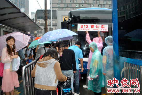 公交志愿者雨中高舉“B12-直達(dá)車(chē)”指示牌疏導(dǎo)返校學(xué)生乘車(chē)