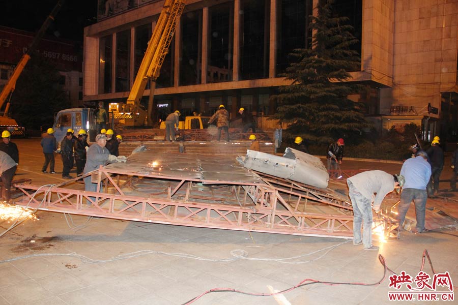 地面上的20多名工人對吊裝下的廣告牌進行分割。