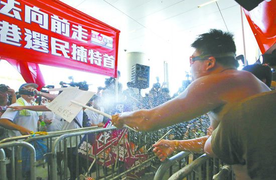 17日，在香港立法會(huì)外，一名反對政改的男子向支持派人群投擲標(biāo)牌。