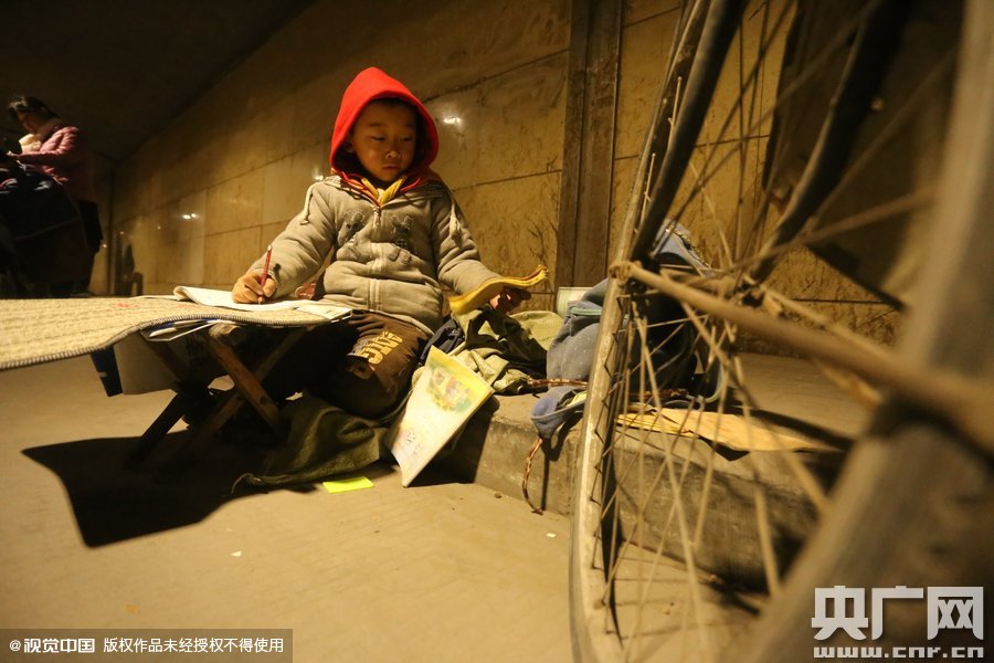 2015年11月8日晚，鄭州，7歲男孩涵洞橋下陪父母練攤，路邊燈下坐小馬扎上寫作業(yè)。