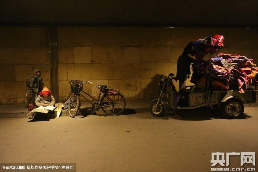 2015年11月8日晚，鄭州，7歲男孩涵洞橋下陪父母練攤，路邊燈下坐小馬扎上寫作業(yè)。