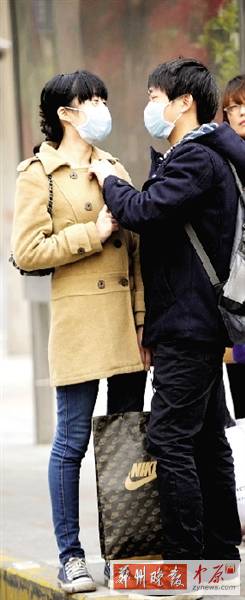 公交站臺上，一對年輕人戴著口罩，系緊衣領(lǐng)。